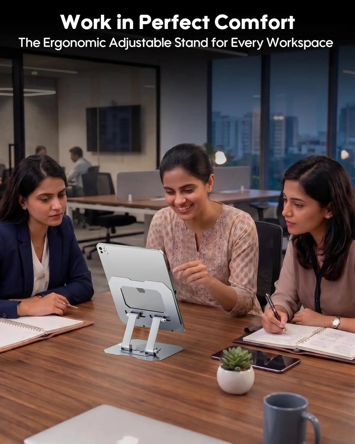 Three women working at a desk with an ergonomic adjustable stand for a tablet, in an office setting.