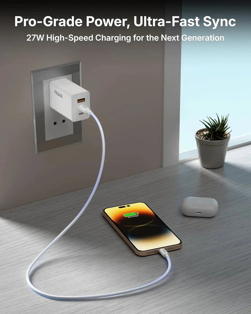 Phone being charged with a cable, next to a wall outlet and plant on a wooden floor.